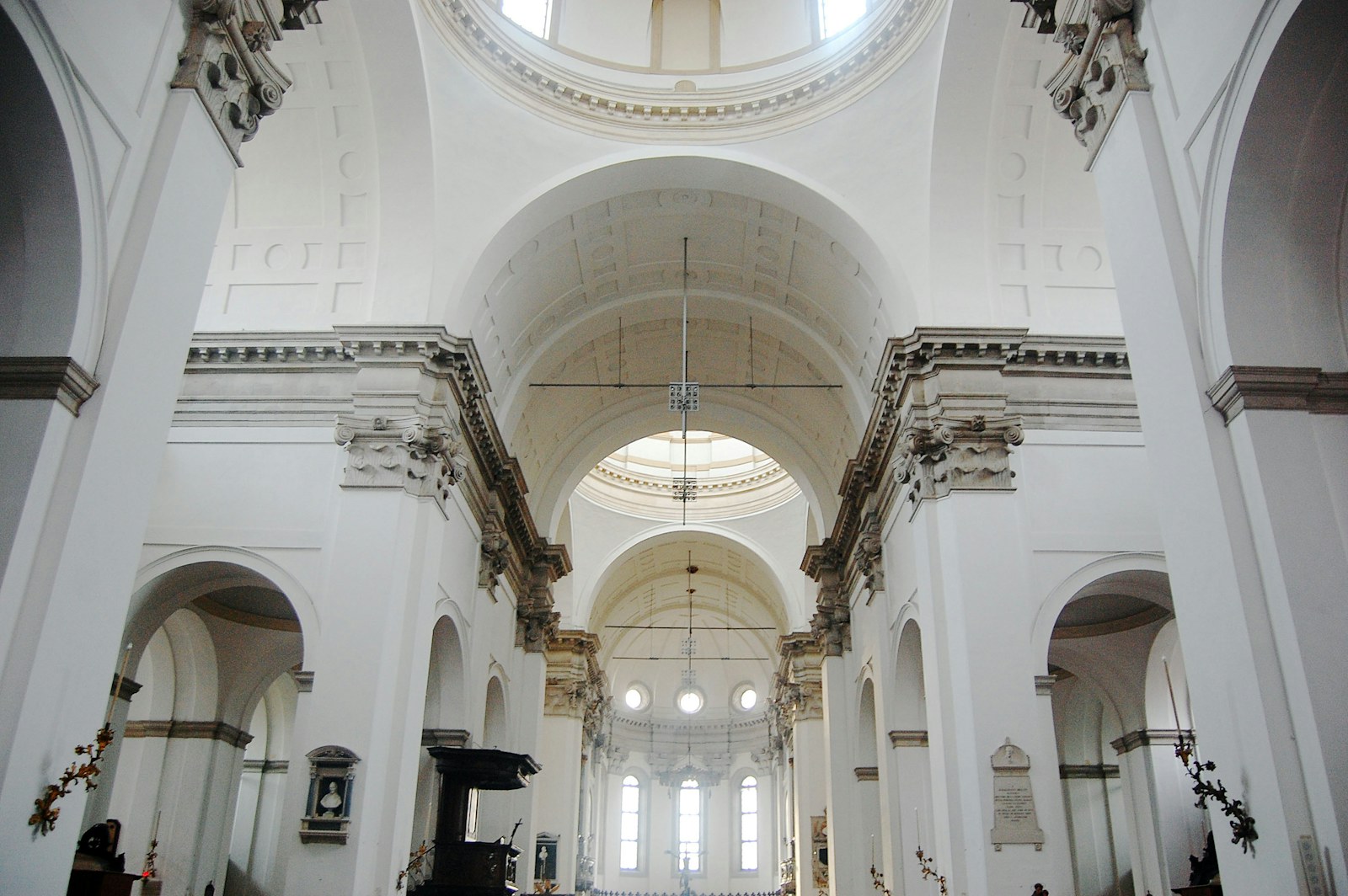 Interior luminoso de una iglesia blanca, con columnas, arcos y una cúpula.